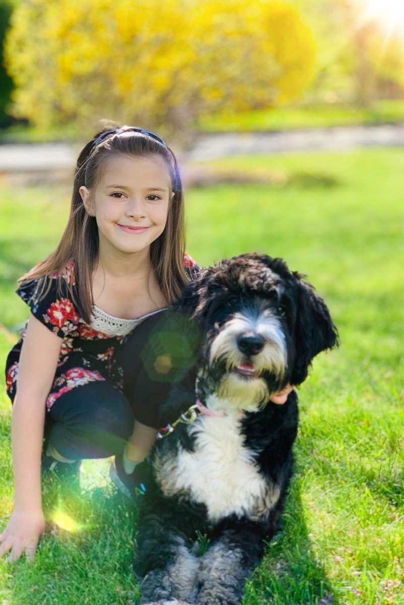 What Sets Us Apart Bernedoodle and a smiling little girl sitting in the grass at Integrity Bernedoodles in Iowa